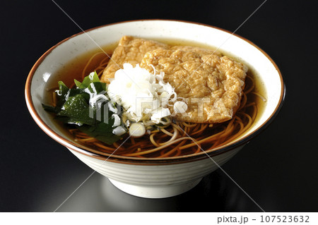 油揚げ2枚とワカメと葱が乗ったきつね蕎麦を黒背景で撮影 油揚げ2枚とワカメと葱が乗ったきつね蕎麦を黒背景で撮影 107523632