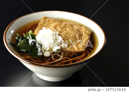 油揚げ2枚とワカメと葱が乗ったきつね蕎麦を黒背景で撮影 107523638