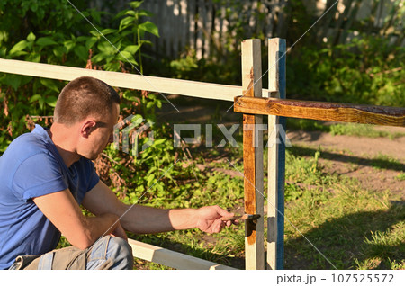 Man outdoors painting wood with a brush 107525572