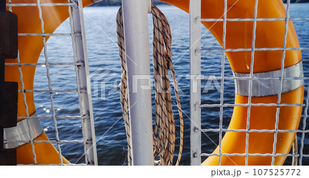 Lifebuoy. View of the water from a pleasure boat. The shine of the sun on the waves creates an atmosphere of safety and joy. Fence, ropes, rescue equipment. Lifebuoy. View of the water from a pleasure boat. The shine of the sun on the waves creates an atmosphere of safety and joy. Fence, ropes, rescue equipment. 107525772