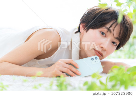 リビングで寝転んでスマホを見るミドルの女性 107525900