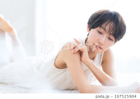 リビングで寝転んでスキンケアをするミドルの女性 リビングで寝転んでスキンケアをするミドルの女性 107525904
