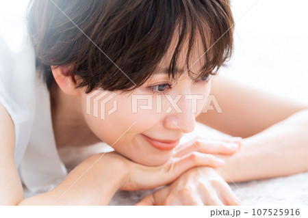リビングで寝転んでスキンケアをするミドルの女性 リビングで寝転んでスキンケアをするミドルの女性 107525916