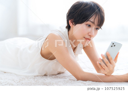 リビングで寝転んでスマホを見るミドルの女性 107525925