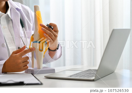 Orthopedist or traumatologist with knee joint model having online consultation on laptop. Telemedicine and healthcare Orthopedist or traumatologist with knee joint model having online consultation on laptop. Telemedicine and healthcare 107526530