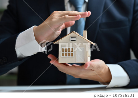 Businessman protecting house model with hands. Real estate and property Insurance concept Businessman protecting house model with hands. Real estate and property Insurance concept 107526531