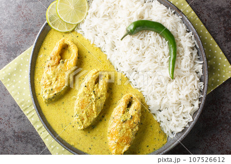 Portion of the popular Hilsa or Ilish fish stewed in mustard sauce with a side dish of white rice close-up in a plate. horizontal top view Portion of the popular Hilsa or Ilish fish stewed in mustard sauce with a side dish of white rice close-up in a plate. horizontal top view 107526612