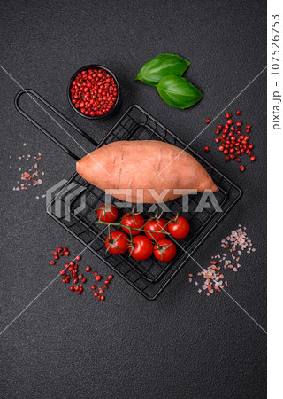 Fresh large pink sweet potato tubers with tomatoes and spices on a dark background 107526753