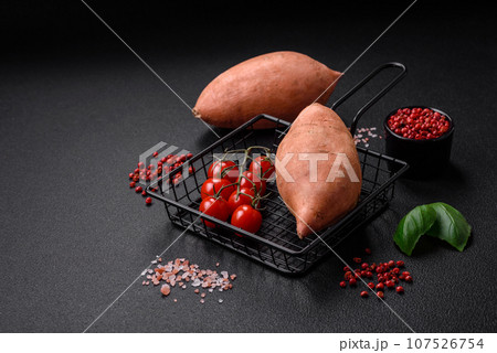 Fresh large pink sweet potato tubers with tomatoes and spices on a dark background 107526754