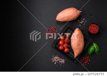 Fresh large pink sweet potato tubers with tomatoes and spices on a dark background Fresh large pink sweet potato tubers with tomatoes and spices on a dark background 107526755