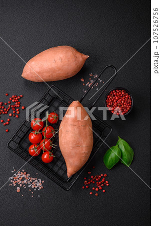 Fresh large pink sweet potato tubers with tomatoes and spices on a dark background Fresh large pink sweet potato tubers with tomatoes and spices on a dark background 107526756