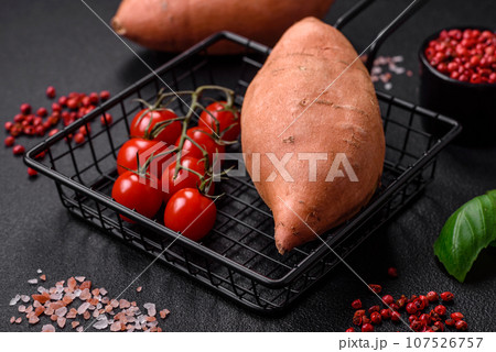 Fresh large pink sweet potato tubers with tomatoes and spices on a dark background Fresh large pink sweet potato tubers with tomatoes and spices on a dark background 107526757