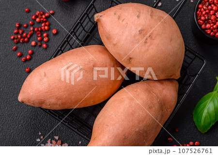 Fresh large pink sweet potato tubers with tomatoes and spices on a dark background 107526761