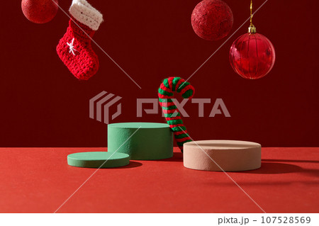 Front view of green and brown podiums decorated with cute red baubles and stock on red background. Space for cosmetic product mockup. Product and promotion concept for advertising Front view of green and brown podiums decorated with cute red baubles and stock on red background. Space for cosmetic product mockup. Product and promotion concept for advertising 107528569