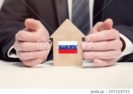 Businessman hand holding wooden home model with Russian flag. insurance and property concepts Businessman hand holding wooden home model with Russian flag. insurance and property concepts 107528755