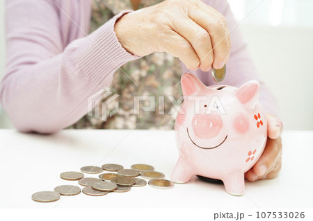 Retired elderly woman putting coins money in piggy bank and worry about monthly expenses and treatment fee payment. Retired elderly woman putting coins money in piggy bank and worry about monthly expenses and treatment fee payment. 107533026