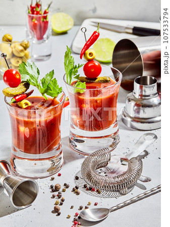 Glasses of bloody mary vodka and tomato juice mix with cocktail utensils on light board. 107533794