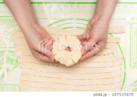An apple ring wrapped in dough in the hands of a young woman. 107535870