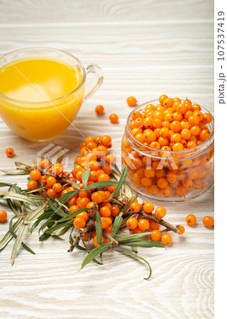 Sea buckthorn healthy hot tea, ripe berries in glass jar and branches with leaves on white wooden rustic background, great for skin, heart, vessels and immune system. 107537419