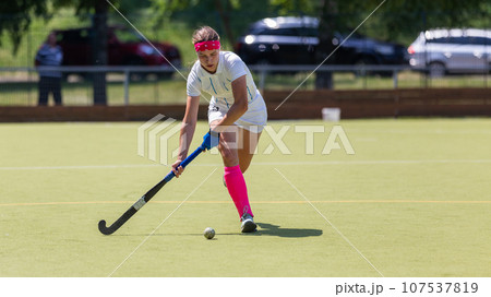 Young female player running with ball in attack on the pitch in field hockey game 107537819