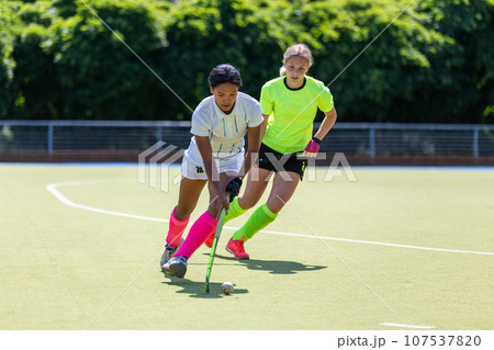 Two female field hockey players fighting for the ball on the pitch in attack Two female field hockey players fighting for the ball on the pitch in attack 107537820