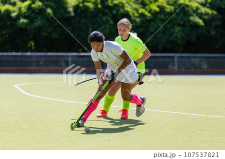 Two female field hockey players fighting for the ball on the pitch in attack Two female field hockey players fighting for the ball on the pitch in attack 107537821