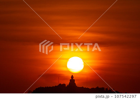 The sun circles in the red sky behind the Big Buddha..Amazing Phuket big Buddha in circle of the sun in red sky..The beauty of the statue fits perfectly with the charming nature. .red sky background 107542297
