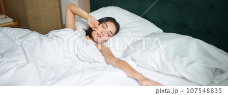 Romantic asian girl waking up in cozy bedroom, lying in bed with white sheets, stretching her hand towards empty pillow Romantic asian girl waking up in cozy bedroom, lying in bed with white sheets, stretching her hand towards empty pillow 107548835