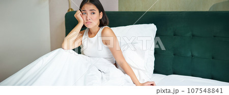Portrait of distressed asian woman lying in bed, looking complicated and upset, cant understand smth, spending time in bedroom 107548841