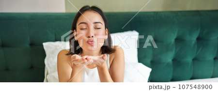 Beautiful korean girlfriend, girl in bed, sending air kiss at camera, lying in bed in her bedroom, waking up early 107548900