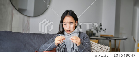 Shocked woman looks concerned at her thermometer, catching cold, has fever, sitting on sick leave at home 107549047