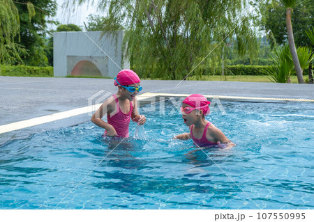 Two little girls swimming and playing in water. Children in swimming pool having fun during family summer vacation. Two little girls swimming and playing in water. Children in swimming pool having fun during family summer vacation. 107550995