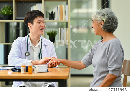 Smiling doctor in white coat holding hand, supporting senior female patient. Medical healthcare concept Smiling doctor in white coat holding hand, supporting senior female patient. Medical healthcare concept 107551948