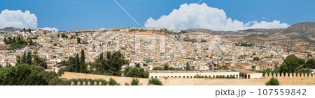 Beautiful panoramic view of the old Medina in Fes, Morocco (Fes El Bali Medina), a sea of buildings made of earthy tones. It's a bustling maze of life, with people and markets nestled in its heart 107559842