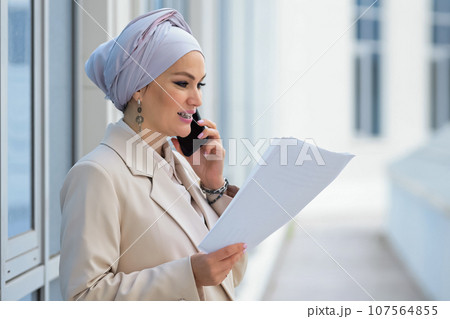 Muslim lady entrepreneur looking at paper talks with client 107564855