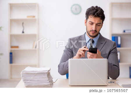 Young male employee and too much work in the office Young male employee and too much work in the office 107565507