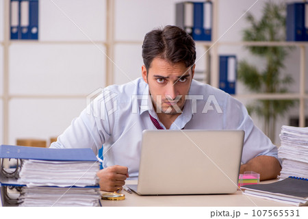 Young male employee and too much work in the office Young male employee and too much work in the office 107565531