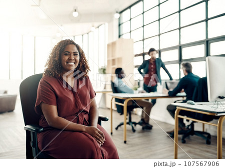 Positivity is the key to success. Portrait of a young businesswoman sitting in a modern office with her colleagues working in the background. 107567906