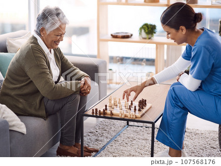 Women, chess and nurse with a senior patient, retirement home and happiness with healthcare. Female person, medical professional and mature lady with employee, nursing and care with games and relax 107568176