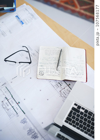 Notebook, laptop and blueprint on desk above for architecture planning, strategy or layout at office. Top view of building paperwork, floor plan or architect notes for construction ideas on workspace 107568177