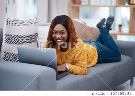 Black woman with laptop, portrait and relax on sofa, search online for movie and streaming subscription at home. Happy African female person in apartment, connectivity and watching on pc with web 107569239