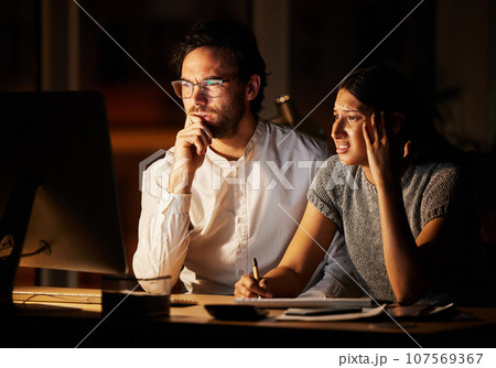 This cant be right.... Shot of two businesspeople looking confused while working together on a computer in an office at night. This cant be right.... Shot of two businesspeople looking confused while working together on a computer in an office at night. 107569367