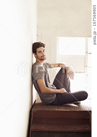 Portrait, relax and stairs with a man sitting by a window on the landing of a staircase while alone in his home. Happy, content and lifestyle with a handsome young male person laid-back in a house Portrait, relax and stairs with a man sitting by a window on the landing of a staircase while alone in his home. Happy, content and lifestyle with a handsome young male person laid-back in a house 107569905