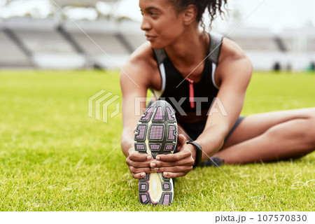 Woman, hands and athlete stretching legs on grass at stadium in preparation for running, exercise or workout. Active or fit female person in warm up leg stretch for fitness, sports or run on field 107570830