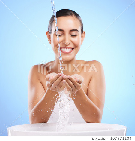 Woman, hands and water splash with smile for skincare hygiene, wash or facial treatment in sink against blue studio background. Happy female smiling in natural beauty cleanse, minerals or self care Woman, hands and water splash with smile for skincare hygiene, wash or facial treatment in sink against blue studio background. Happy female smiling in natural beauty cleanse, minerals or self care 107571104