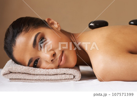 Portrait of woman, rock or back massage in spa to relax for zen, resting or wellness physical therapy. Face of girl client in salon to exfoliate for skincare healing treatment or hot stone therapy 107571399