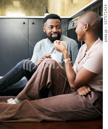 Conversation, happy and African couple with coffee for peace, love and care on the kitchen floor. Communication, smile and black man and woman drinking tea while talking about their relationship 107571424