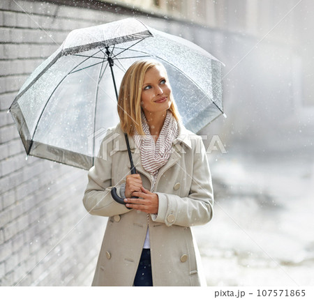 Enjoying a walk in the rain. Shot of a young woman walking down the street with an umbrella on a rainy day. Enjoying a walk in the rain. Shot of a young woman walking down the street with an umbrella on a rainy day. 107571865