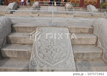 Dragon symbol of stone of the traditional ancient old wooden Junghwajeon Hall of Deoksugung palace with colourful trees foliage in Autumn. There are many tourists in the photo. 107571902