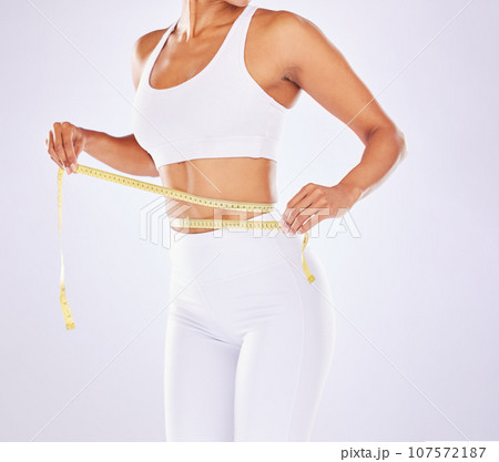 Health, waist and tape measure for diet of woman in studio for healthy lifestyle, weight loss or fitness. Female on a white background for health, wellness and stomach motivation for healthcare goals Health, waist and tape measure for diet of woman in studio for healthy lifestyle, weight loss or fitness. Female on a white background for health, wellness and stomach motivation for healthcare goals 107572187